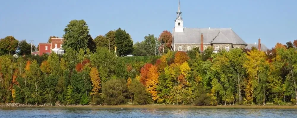 Saint-Pierre-les-Becquets vu du fleuve : le clocher, les érables d’automne et la rive.